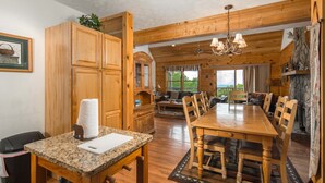 A wooden interior with a dining table, chairs, a kitchen area, and a balcony with a view. - Sleeps 10 | Hot Tub, Game Room, Mountain Views & Near Beech Ski Resort (Beech Mountain)