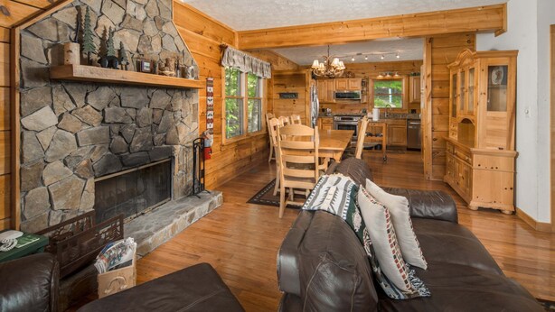 A cabin interior with a stone fireplace, wooden furniture, and a kitchen area. - Sleeps 10 | Hot Tub, Game Room, Mountain Views & Near Beech Ski Resort (Beech Mountain)