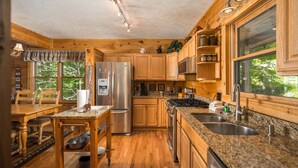 A wooden cabin kitchen with a granite countertop, stainless steel appliances, and a large window. - Sleeps 10 | Hot Tub, Game Room, Mountain Views & Near Beech Ski Resort (Beech Mountain)