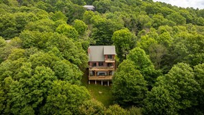 A two-story house surrounded by dense forest, with a visible deck and a small lawn. - Sleeps 10 | Hot Tub, Game Room, Mountain Views & Near Beech Ski Resort (Beech Mountain)