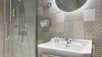 A modern bathroom with a glass-enclosed shower, a pedestal sink, and patterned tiles.