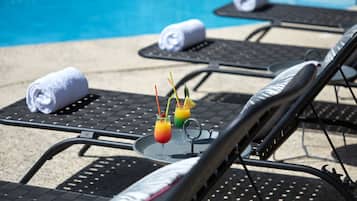 A poolside lounge area with sun loungers, towels, and a tray with drinks.