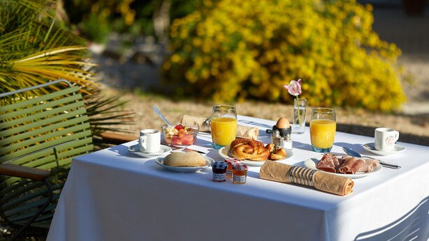 Mesa de café da manhã montada ao ar livre, com diversos alimentos, como doces, frutas e bebidas.