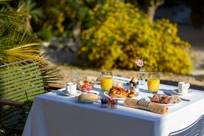 Een ontbijttafel buiten, gedekt met diverse soorten eten, zoals gebak, fruit en drankjes.