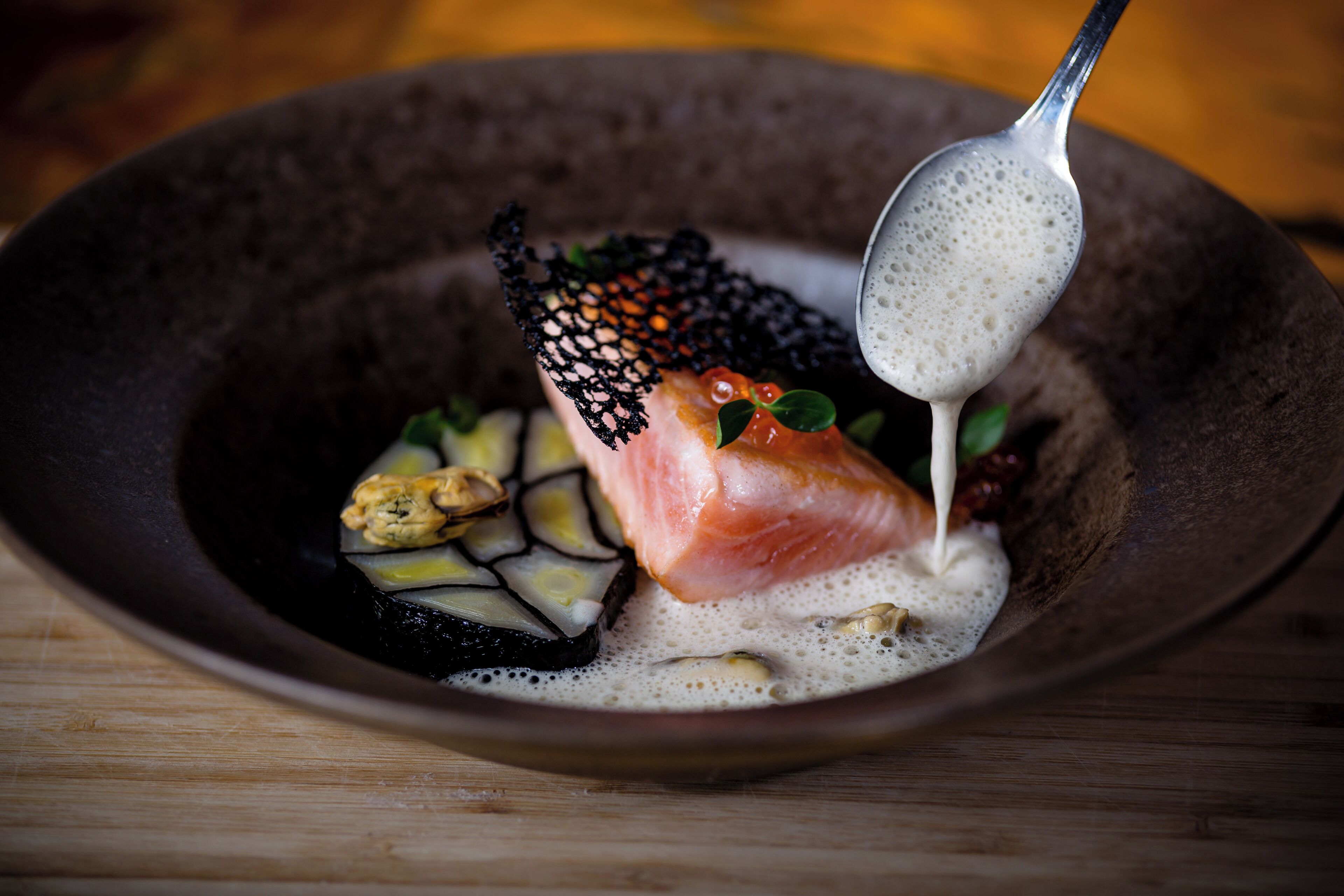 Ein Gericht mit Lachs, schwarzem Kaviar und einer cremigen Soße in einer dunklen Schüssel.
