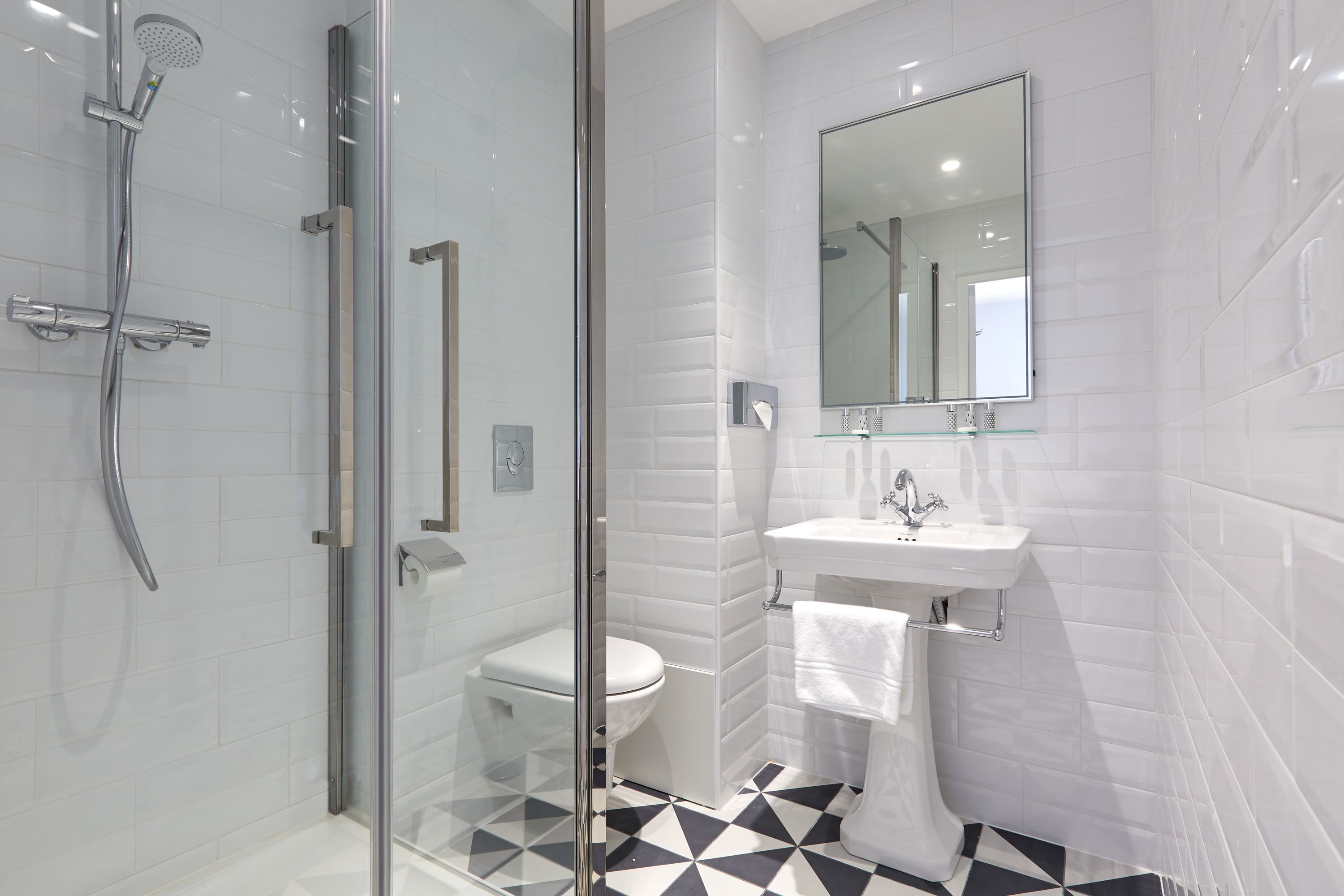 Un baño moderno con cabina de ducha de vidrio, inodoro blanco y lavamanos con espejo.