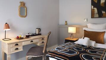 A hotel room with a bed, a desk with a lamp, a chair, a nightstand with a lamp, and a wall-mounted mirror.