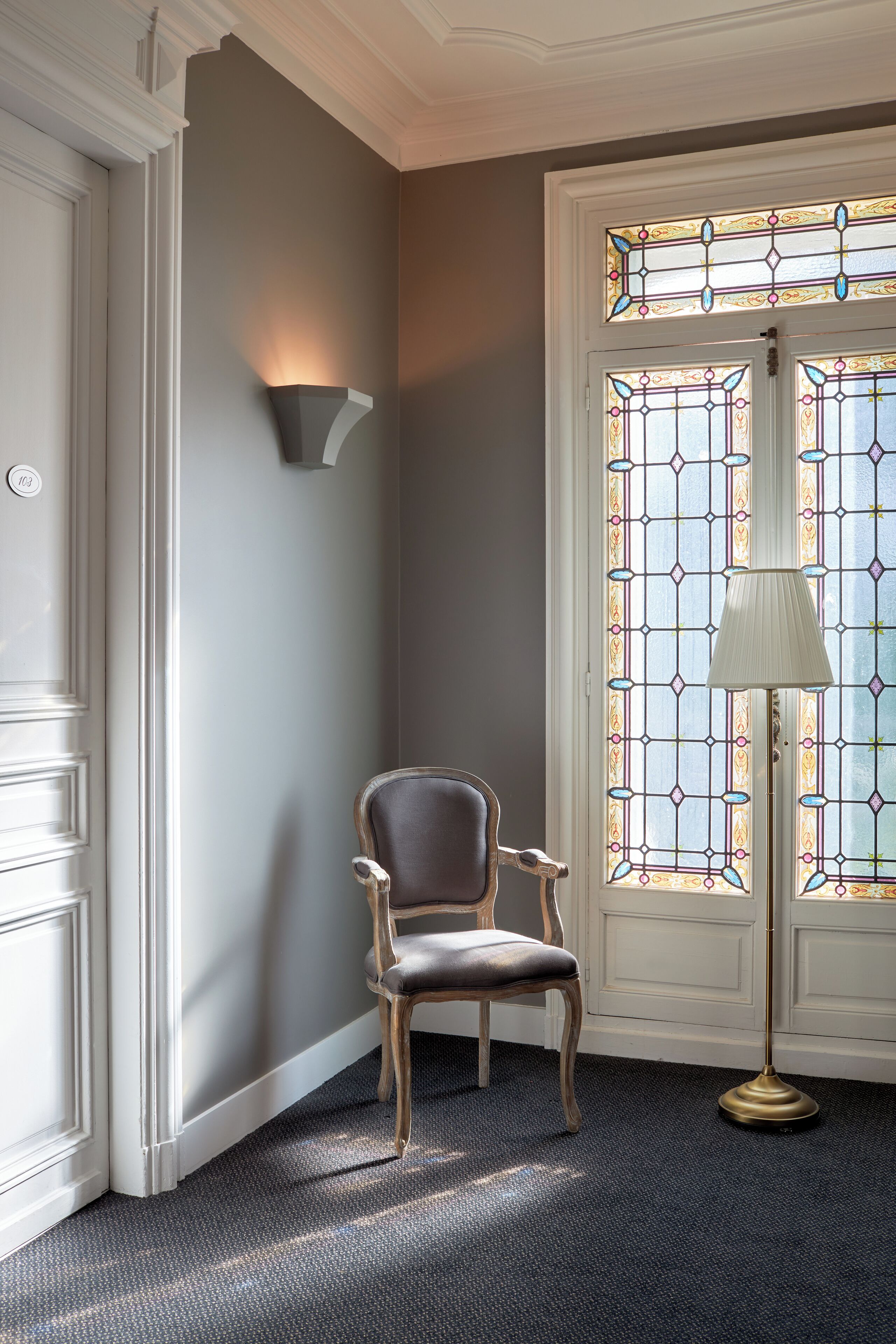 A corner room with a chair, a lamp, and a door with stained glass windows.