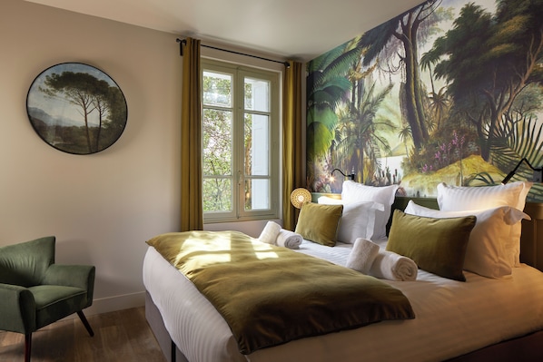 Une chambre d’hôtel avec un lit, une chaise, une fenêtre avec des rideaux et une grande fresque représentant une forêt sur le mur.