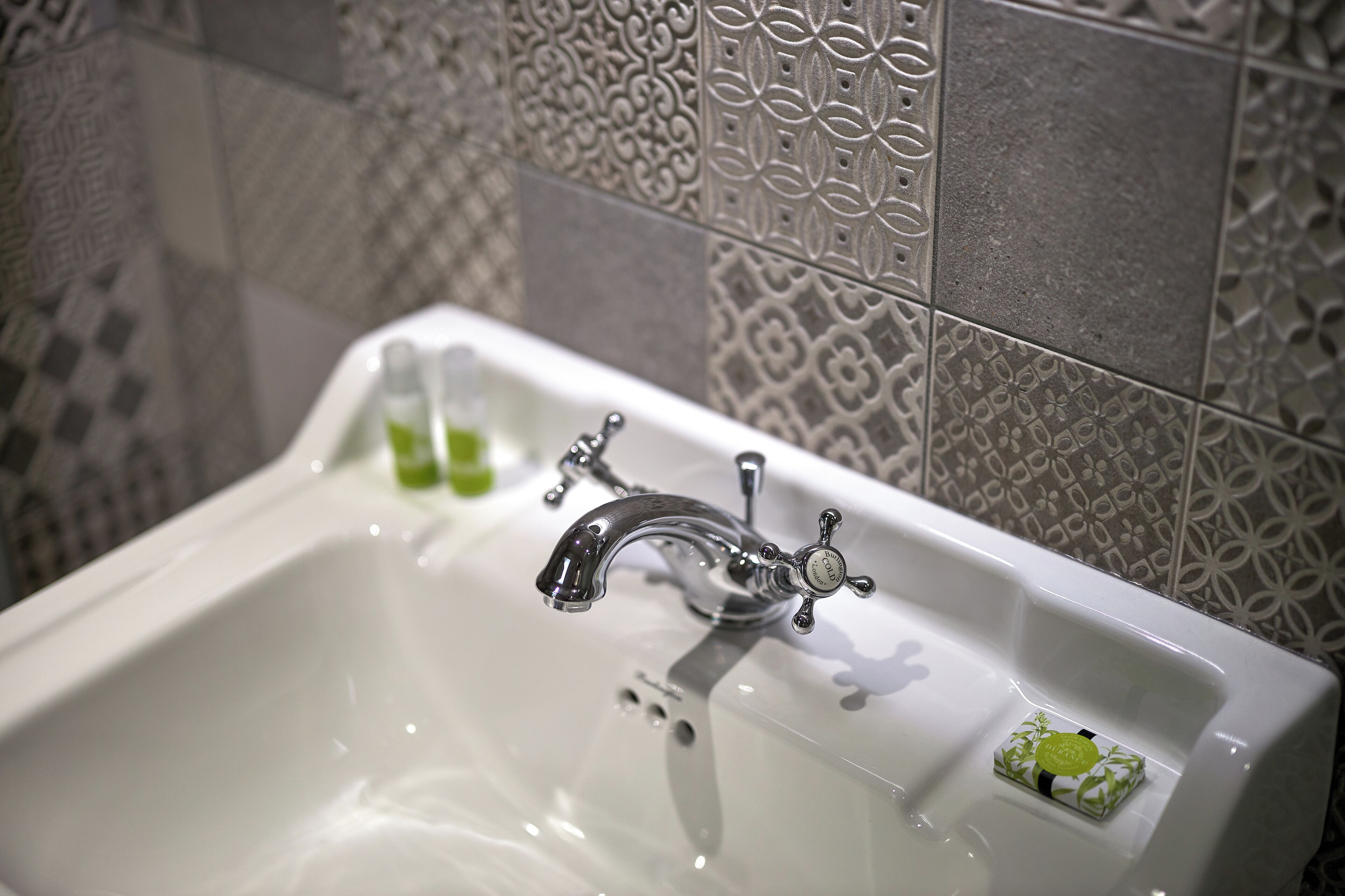 Un baño con un lavabo blanco, un grifo cromado y azulejos decorativos en la pared.