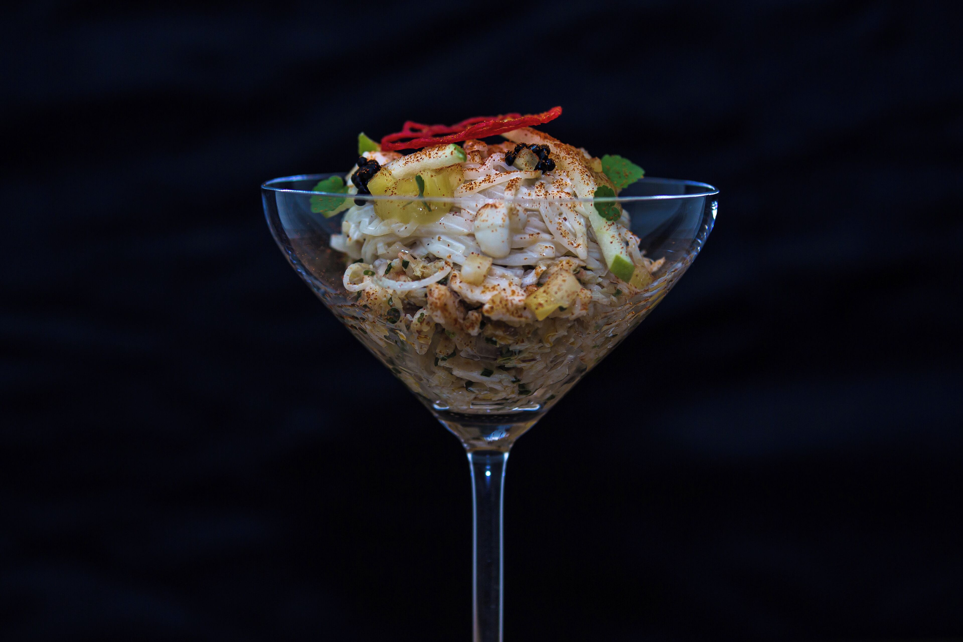 A glass bowl filled with a layered dish, possibly a salad or appetizer, with various ingredients and garnishes.