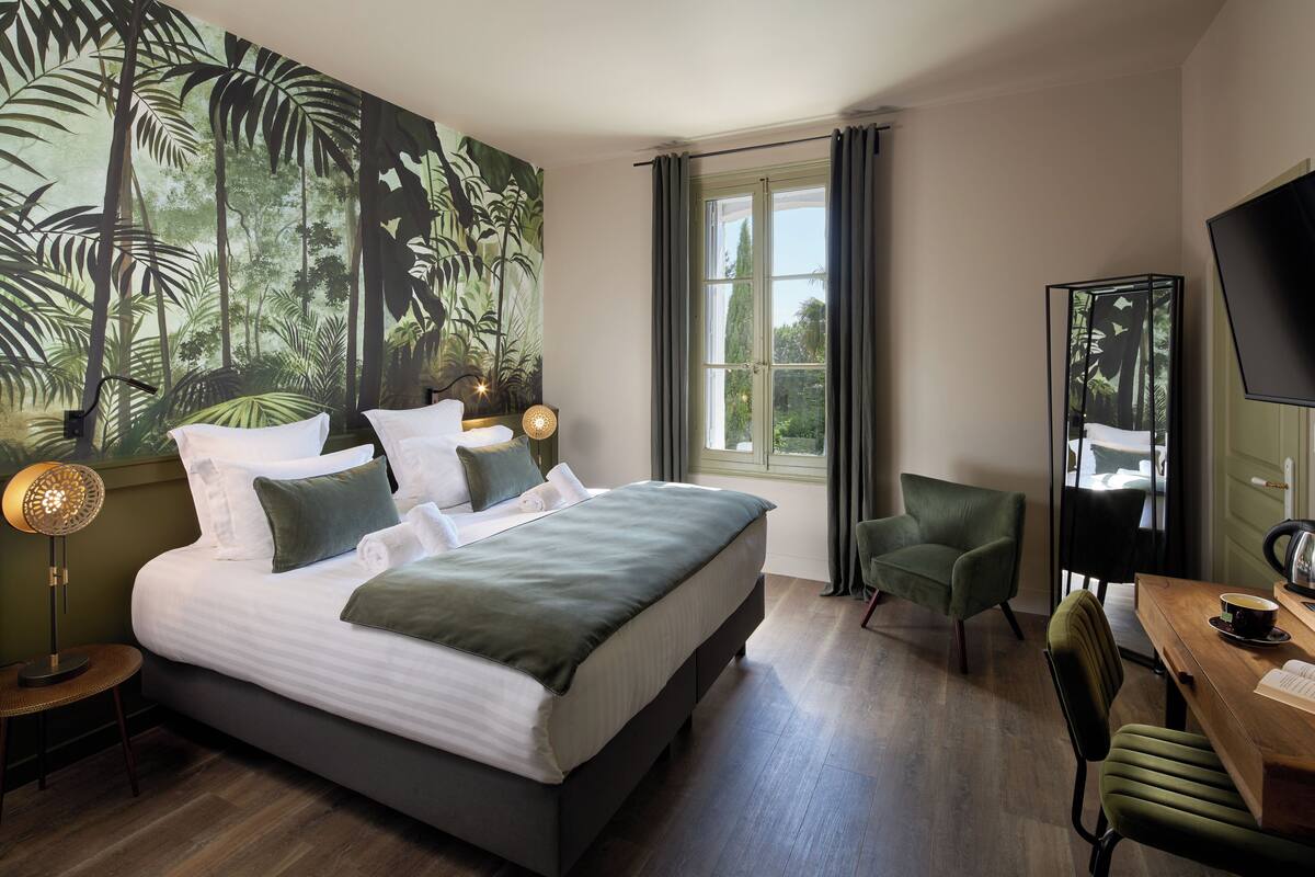 A bedroom with a large bed, a desk, a chair, a TV, and a window with curtains.