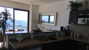 A modern kitchen with a large window overlooking the sea, a built-in oven, and a countertop with kitchenware.