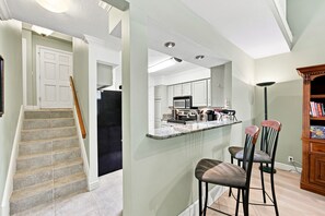 A modern kitchen with a central island, bar stools, and a dining area with a bookshelf.