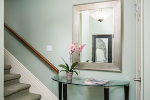 Un escalier avec une rampe en bois, une console en verre sur laquelle sont posés un pot de plantes et des magazines, et une œuvre d’art encadrée représentant un éléphant, accrochée au mur.