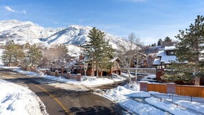 Un quartier résidentiel enneigé, avec des maisons, une route et une montagne en arrière-plan.