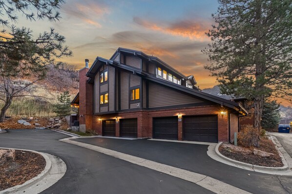 Una casa a due piani con garage, vialetto e alberi circostanti.