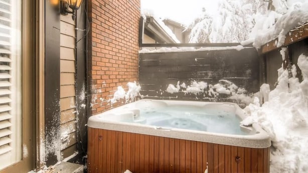 Un bain à remous en bois, avec un mur en briques et une clôture en bois, le tout entouré de neige.