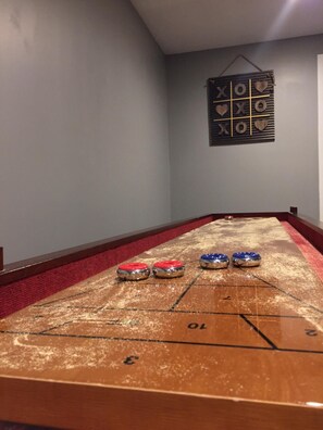 A shuffleboard table with three pucks in red, blue, and silver, and a wall-mounted game board with 'X' and 'O' markers. - Large 2BR Near Pineview, Powder Mtn & Snowbasin Hot Tub (Eden)