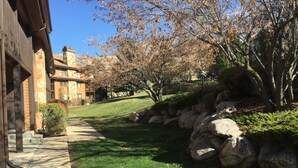 Un edificio con fachada de piedra, un camino empedrado y un área verde con rocas y árboles.