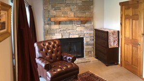 Una sala de estar con chimenea de piedra, un sillón de cuero, un mueble de madera y una puerta.