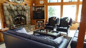 A cozy living room with a stone fireplace, a large sofa, two armchairs, and a coffee table.