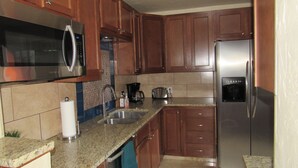 Una cocina con gabinetes de madera, electrodomésticos de acero inoxidable, encimera de granito y salpicadero azulejado.