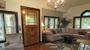 Una sala de estar con una puerta de madera, un sillón color beige, un sofá y una mecedora de madera.