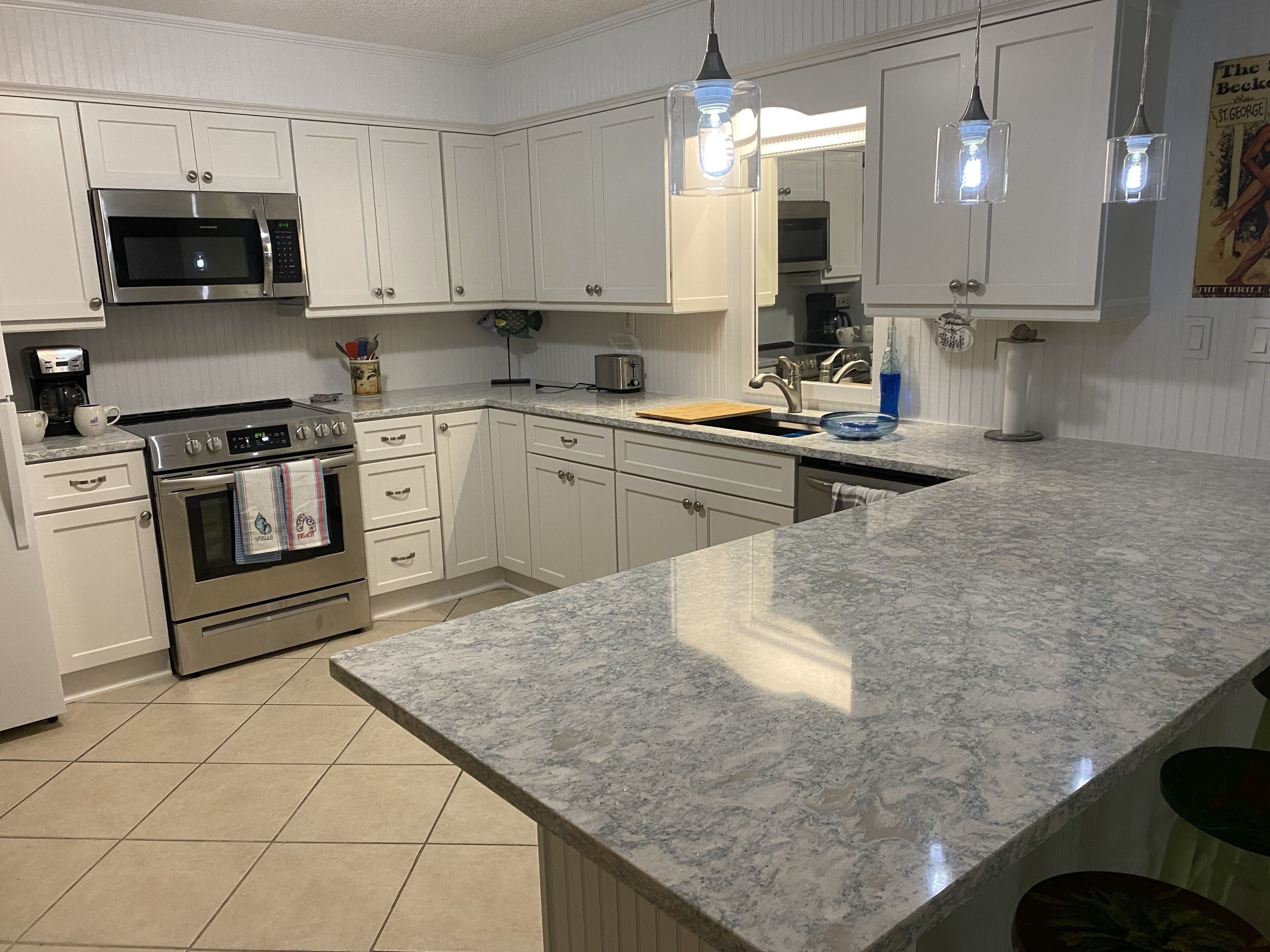 A modern kitchen with white cabinets, stainless steel appliances, a granite countertop, and pendant lighting.