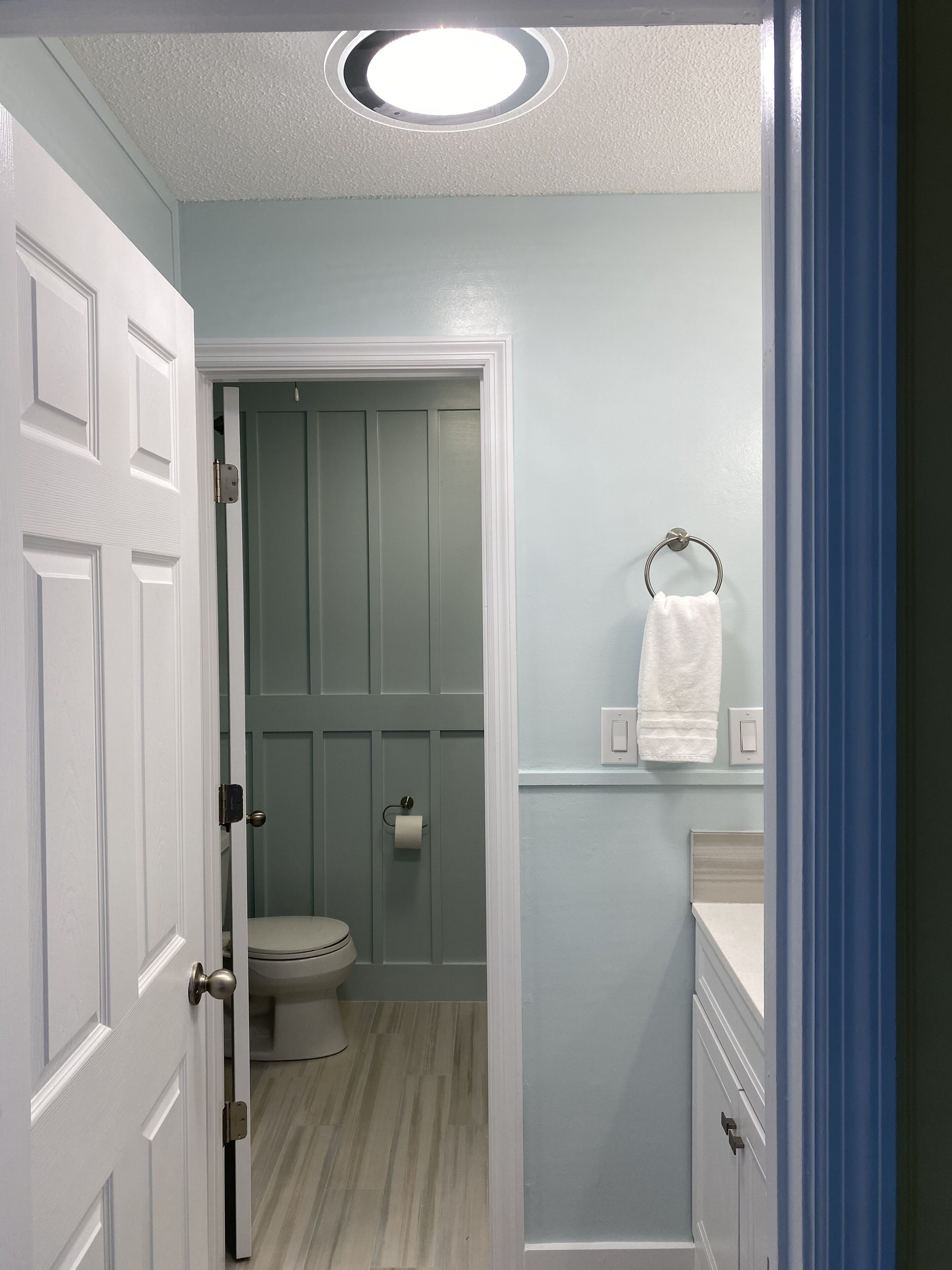 Un baño con inodoro, aro para toallas y un interruptor de luz en la pared.