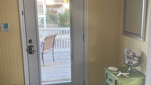 A room with a door leading to a balcony, a small table with decorative items, and a welcome mat.