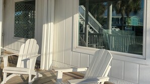 A covered porch with two Adirondack chairs and a large window overlooking a staircase and a blue house.