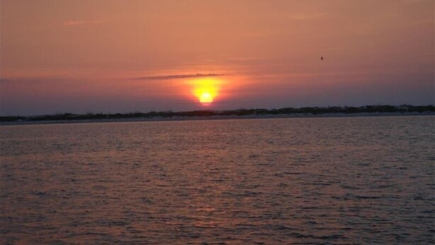 A sunset over a calm body of water with a distant shoreline.