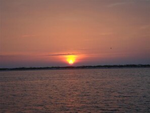 Um pôr do sol sobre águas calmas, com uma linha de costa distante.