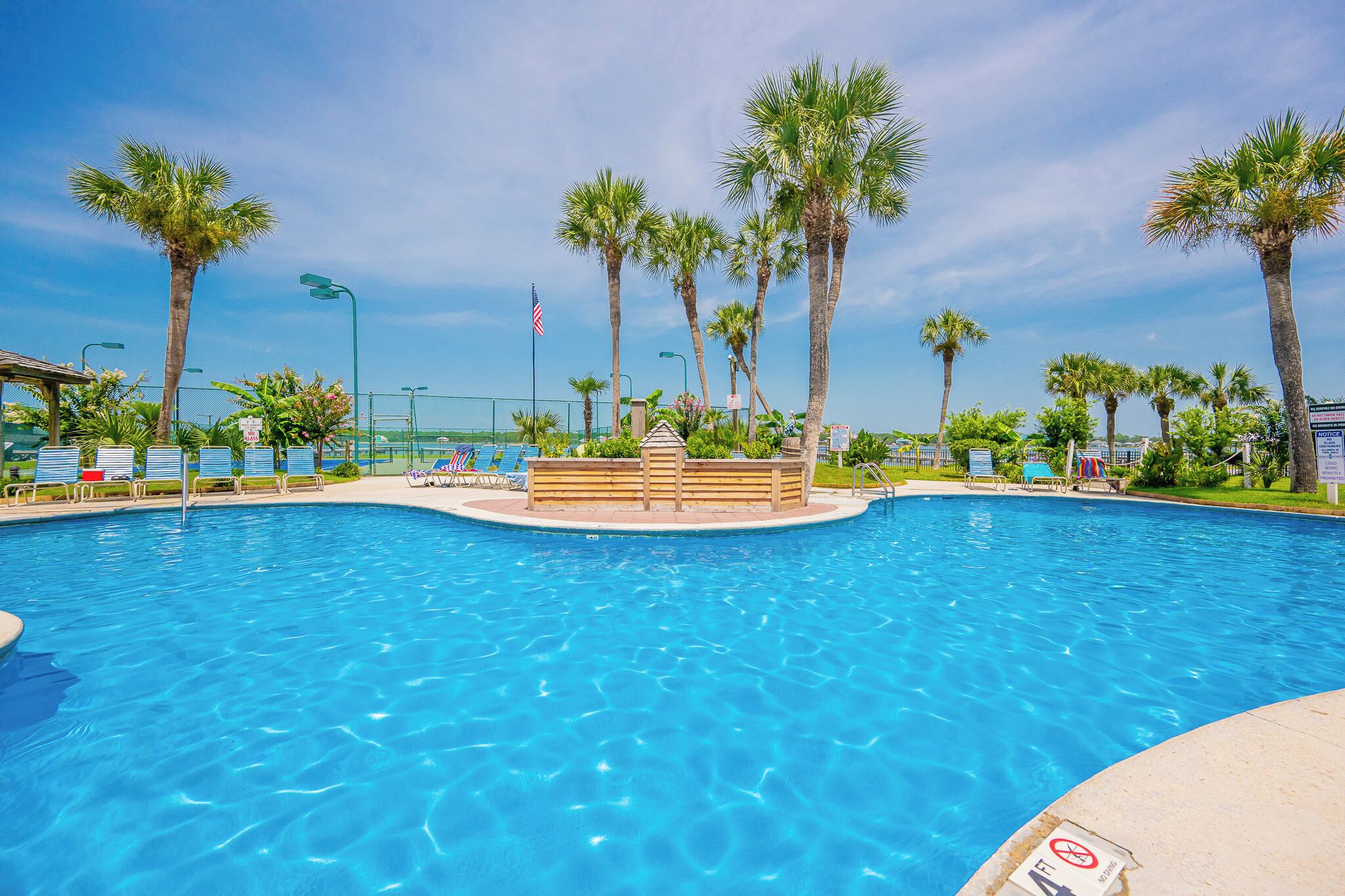 A swimming pool with clear blue water, surrounded by palm trees and lounge chairs.