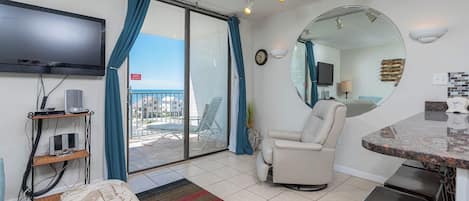 A room with a TV, a chair, a table, a mirror, and a view of the sea.