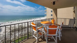A balcony with a view of a beach and ocean. There are two tables and four chairs. - Phoenix I - 2 Bedroom (Orange Beach)