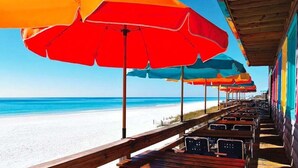 Een restaurant aan het strand met terras en kleurrijke parasols.