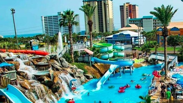 Een waterpark met meerdere glijbanen en zwembaden, omringd door palmbomen en gebouwen.