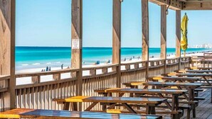 Een houten terras met picknicktafels met uitzicht op een strand.