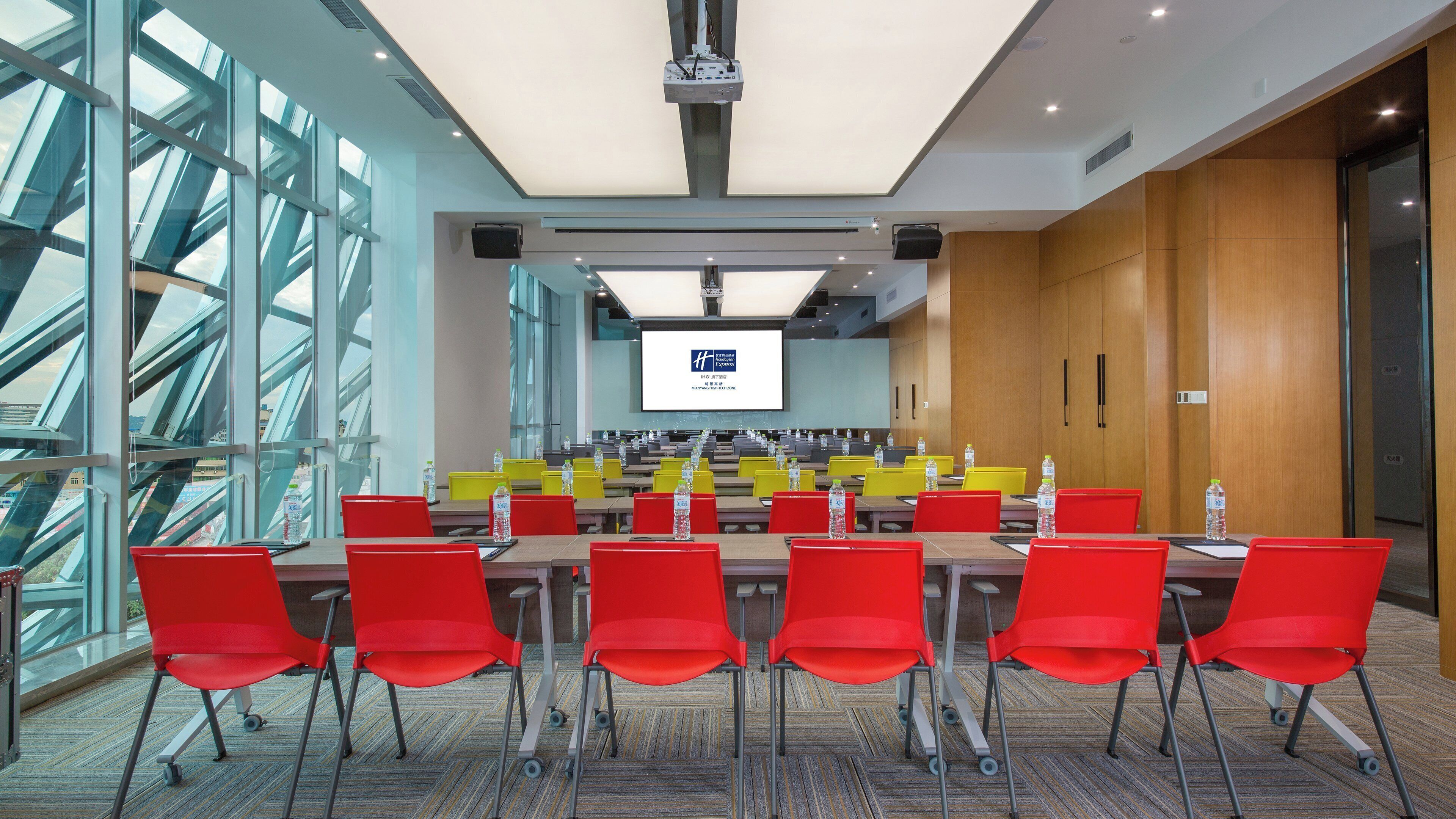 A conference room with a large screen, red chairs, and tables arranged for meetings.