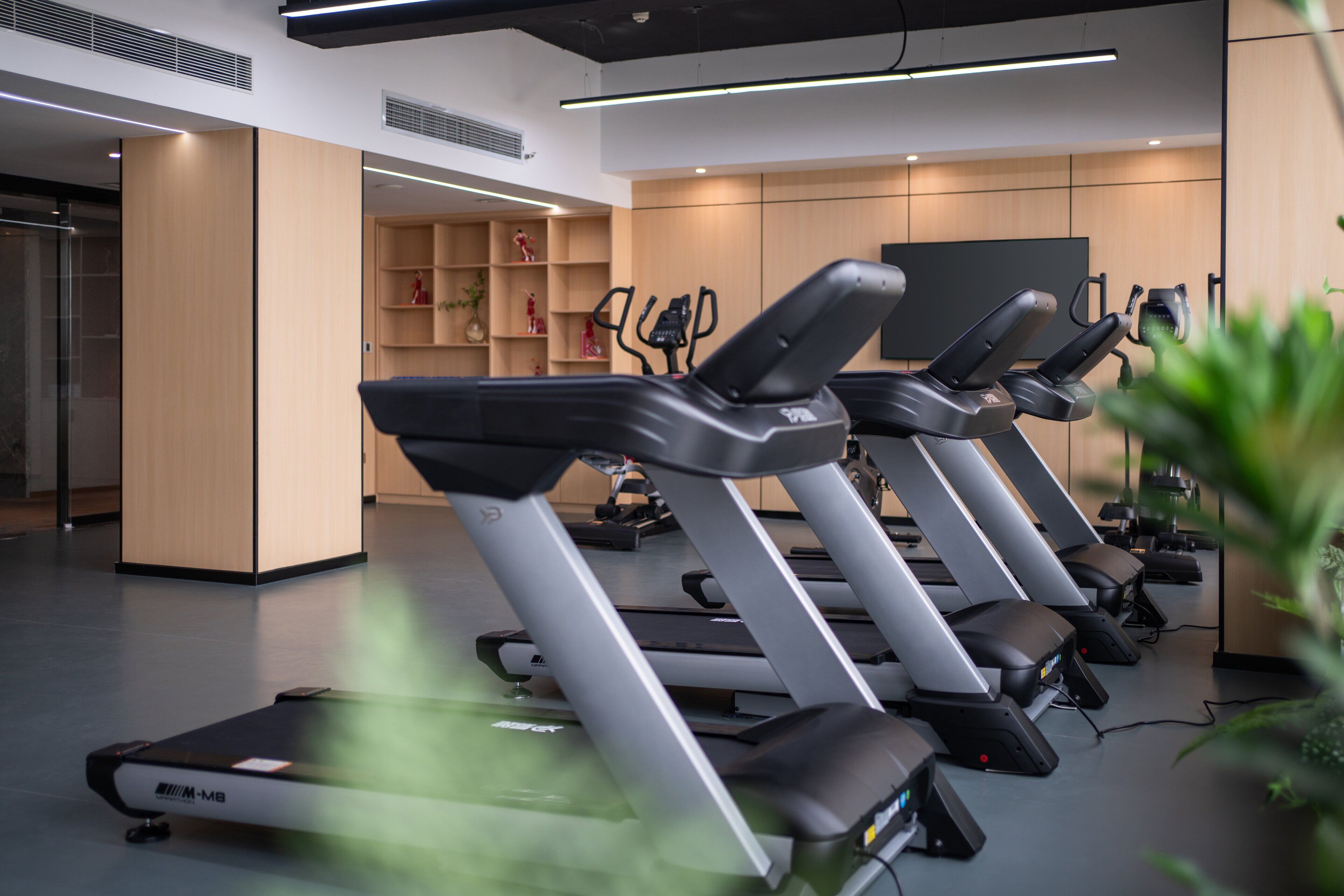 A gym with multiple treadmills, wooden walls, and shelves with decorative items.