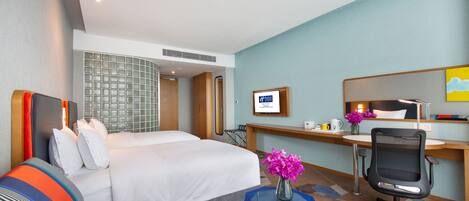 A hotel room with a bed, a desk, a chair, a small table, and a mirror.