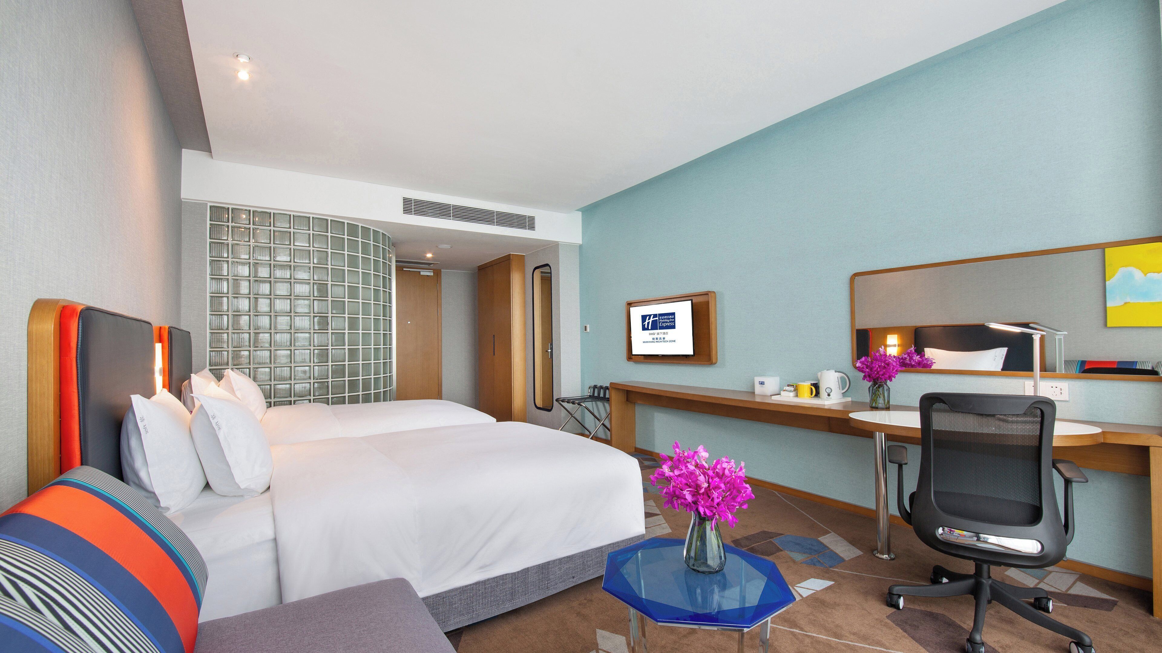 A hotel room with a bed, a desk, a chair, a small table, and a mirror.