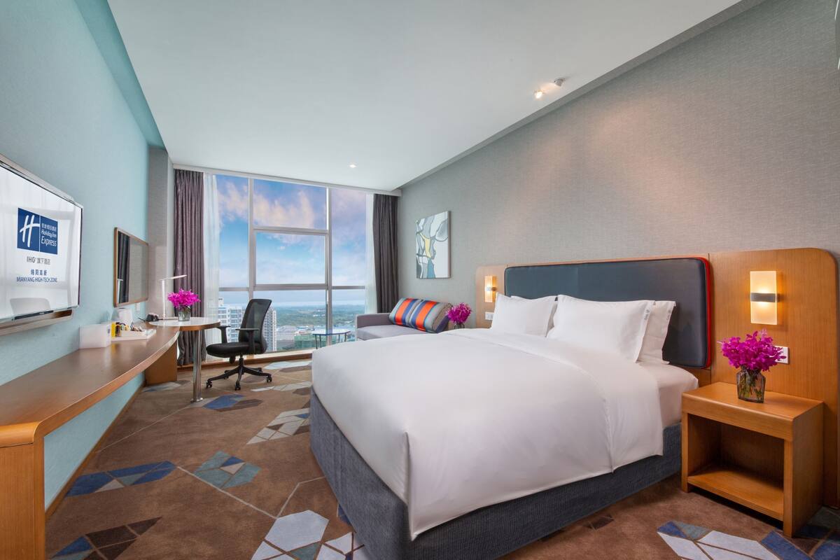 Ein Hotelzimmer mit einem großen Bett, einem Schreibtisch, einem Sessel und einem Fernseher.