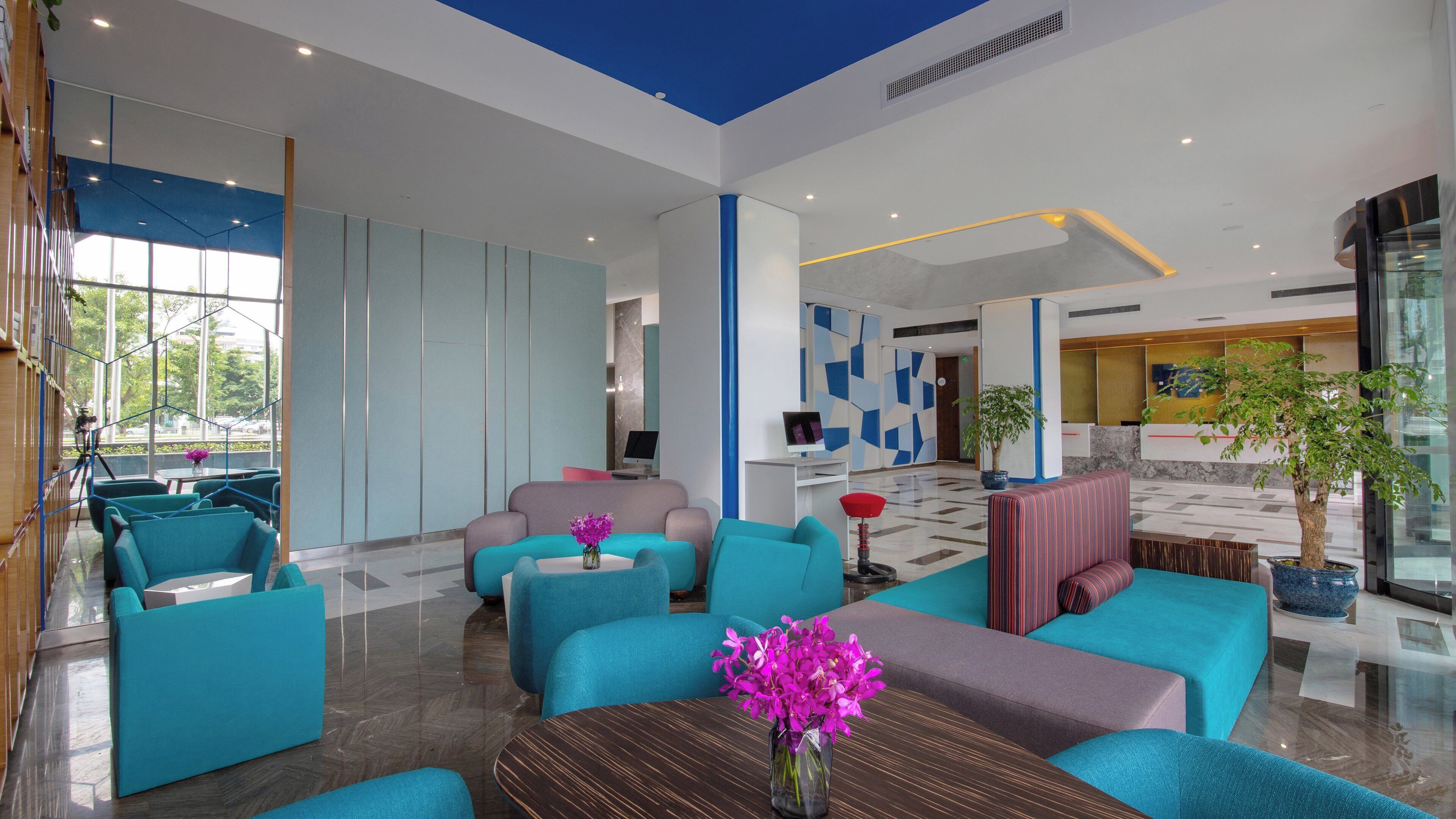 A modern lobby with teal sofas, a coffee table with a vase of flowers, and a reception desk.