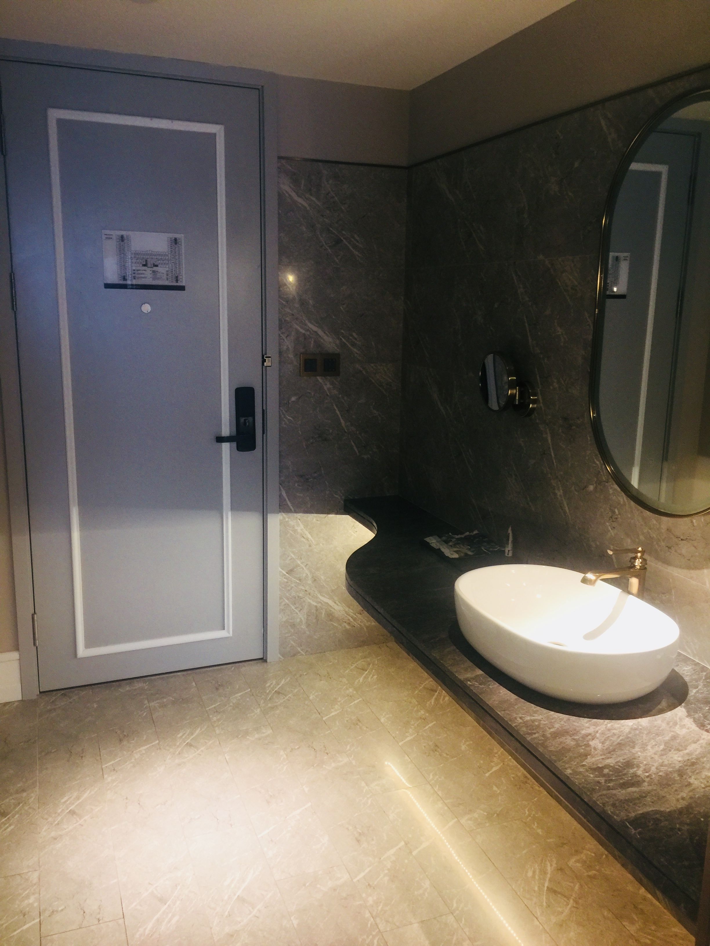 A modern bathroom with a marble sink, a large mirror, and a door with a frosted glass panel.