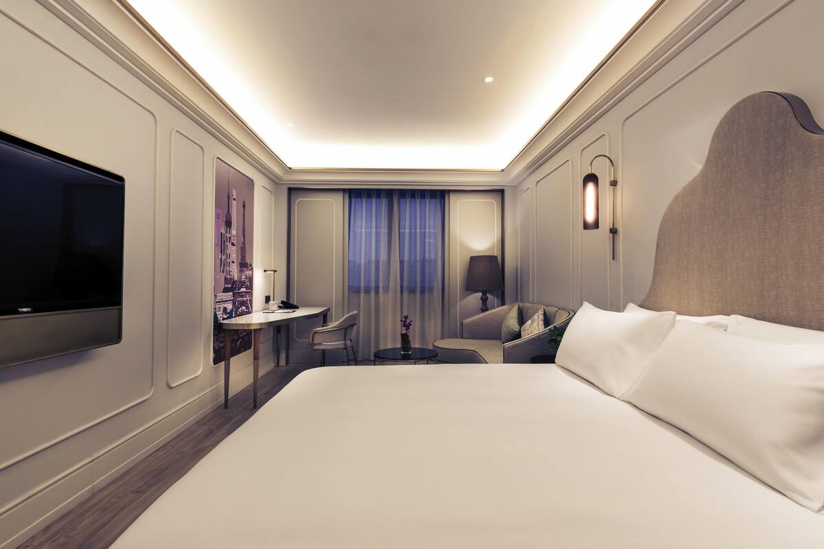 Una habitación de hotel moderna con una cama grande, un escritorio, una silla, un televisor y una lámpara.