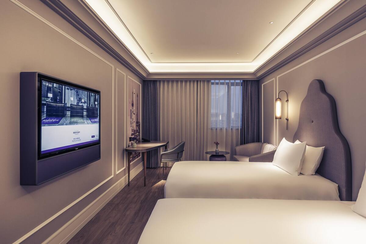 Habitación de hotel con una cama grande, un escritorio, una silla, un televisor y una ventana con cortinas.