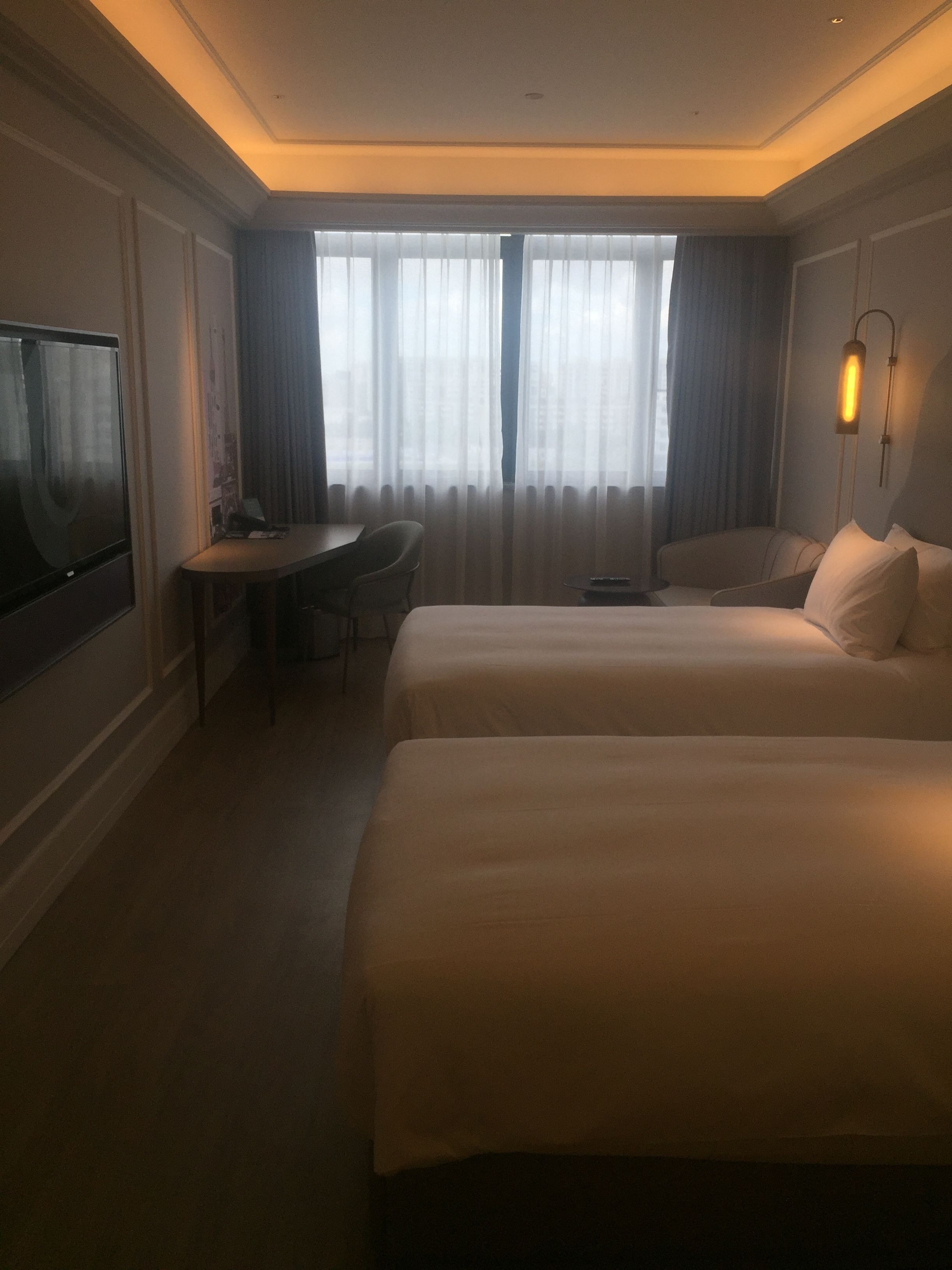 Habitación de hotel con dos camas, un escritorio, una silla, un televisor y una ventana con cortinas.